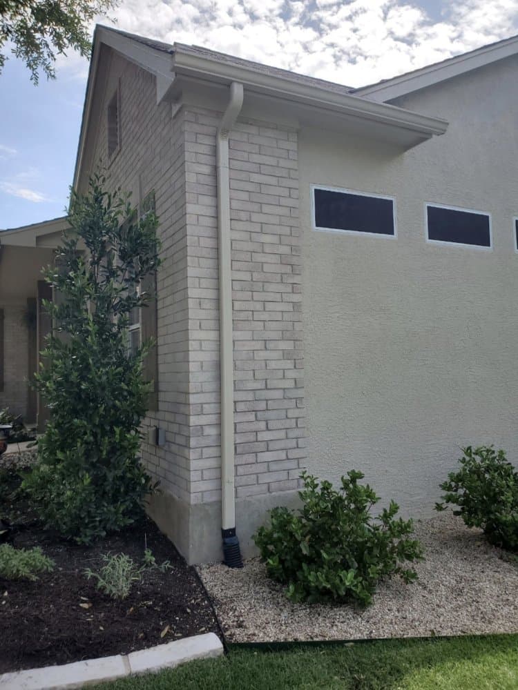 White downspout installed along brick and stucco home
